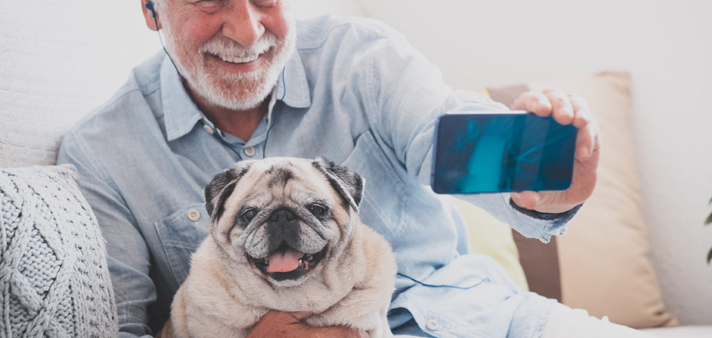 An older adult man takes a selfie with his dog