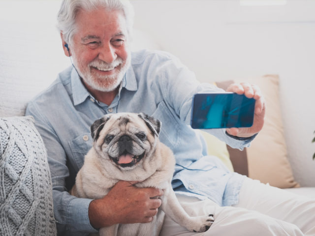 An older adult man takes a selfie with his dog