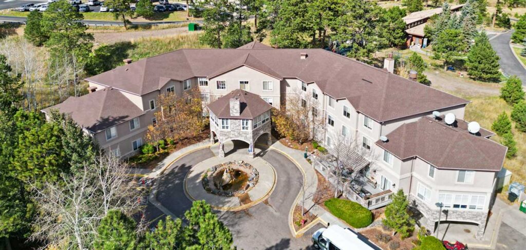 Aerial view of Elk Run Assisted Living in Evergreen, Colorado, showing the building entrance, circular driveway, and surrounding mountain landscape with trees and open space.