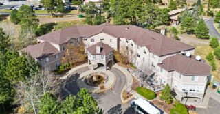Aerial view of Elk Run Assisted Living in Evergreen, Colorado, showing the building entrance, circular driveway, and surrounding mountain landscape with trees and open space.