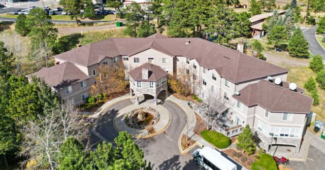 Aerial view of Elk Run Assisted Living in Evergreen, Colorado, showing the building entrance, circular driveway, and surrounding mountain landscape with trees and open space.
